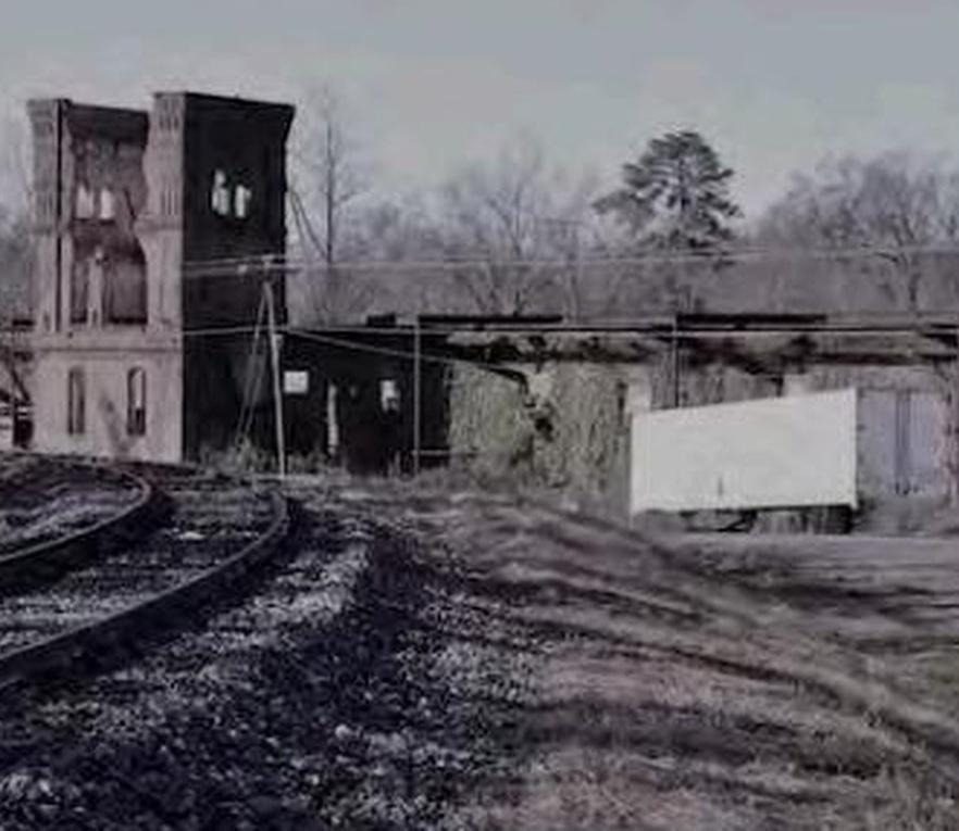 A black-and-white photograph of the former Anderson Cotton Mill site, with brick towers, ruins, and railroad tracks.